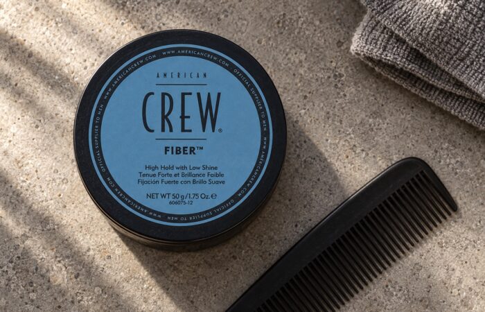 American Crew Fiber 50 g z niebieską etykietą na kamiennym blacie obok czarnego grzebienia.