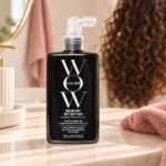 Czarna butelka Color Wow Dream Coat for Curly Hair 200 ml na jasnej toaletce, z lokami w tle