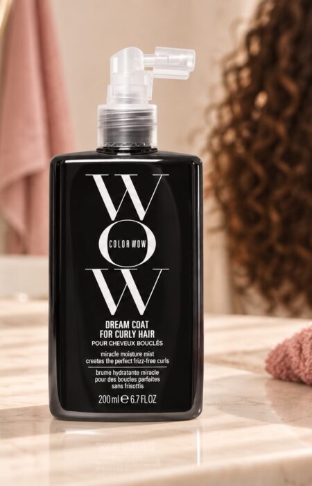 Czarna butelka Color Wow Dream Coat for Curly Hair 200 ml na jasnej toaletce, z lokami w tle