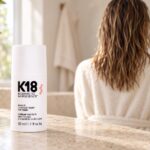 Białe opakowanie maski K18 50 ml na jasnym blacie, w tle wilgotne włosy