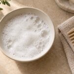 Delikatna piana w jasnej ceramicznej miseczce obok grzebienia i bawełnianego ręcznika.