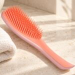 Koralowo-różowa szczotka Tangle Teezer Wet Detangler obok jasnego ręcznika na kamiennym blacie