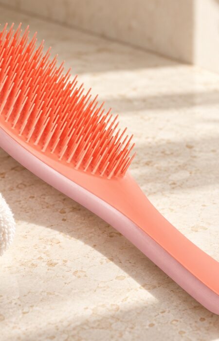 Koralowo-różowa szczotka Tangle Teezer Wet Detangler obok jasnego ręcznika na kamiennym blacie
