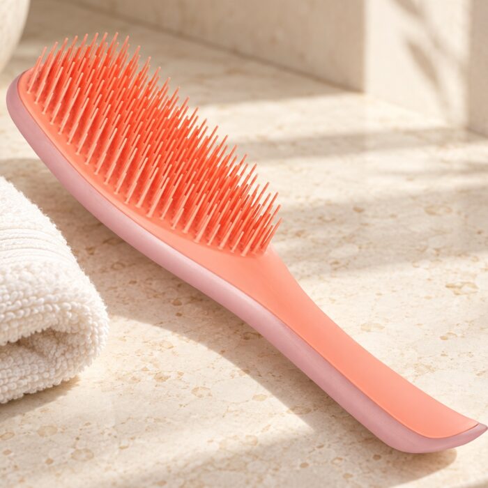 Koralowo-różowa szczotka Tangle Teezer Wet Detangler obok jasnego ręcznika na kamiennym blacie