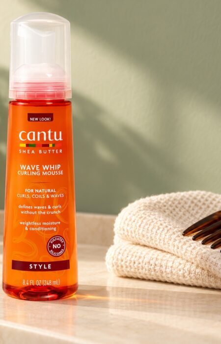 Pomarańczowa butelka Cantu Wave Whip Curling Mousse 248 ml obok ręcznika i grzebienia