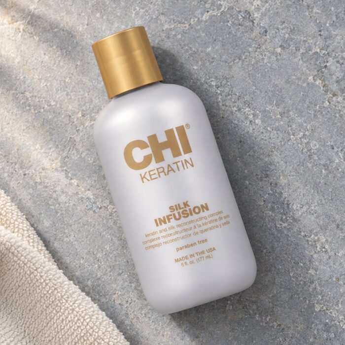 Butelka CHI Keratin Silk Infusion 177 ml ze złotą nakrętką obok ręcznika