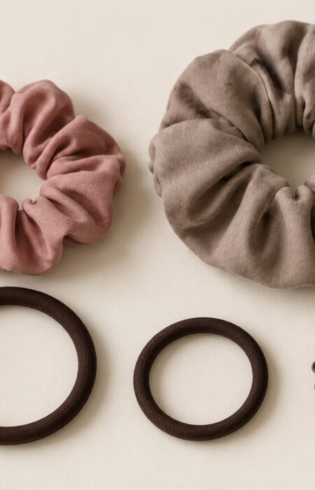 Dwie materiałowe scrunchie, dwie gumki w osłonie i brązowa spiralka ułożone na jasnym tle.