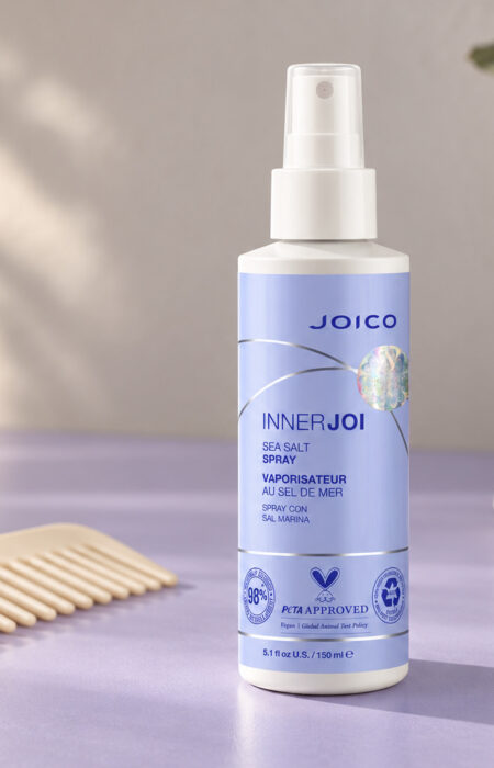 Joico InnerJoi Sea Salt Spray 150 ml z lawendową etykietą obok grzebienia na jasnym blacie.