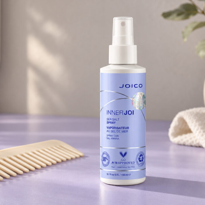 Joico InnerJoi Sea Salt Spray 150 ml z lawendową etykietą obok grzebienia na jasnym blacie.