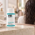 Butelka K18 Peptide Prep Detox Shampoo 250 ml obok ręcznika, z wilgotnymi włosami w tle