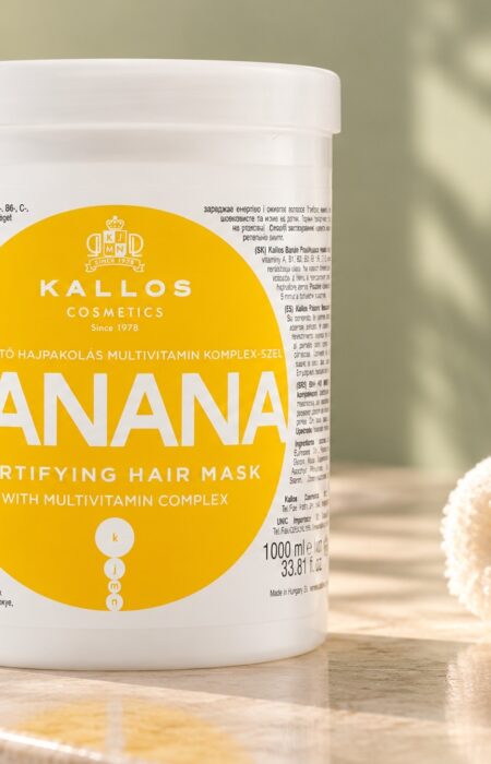 Biały słoik maski Kallos Banana z żółtą etykietą obok jasnego ręcznika