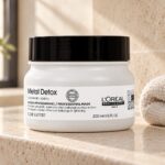 Słoik maski L’Oréal Metal Detox 250 ml z czarną pokrywką obok złożonego ręcznika.