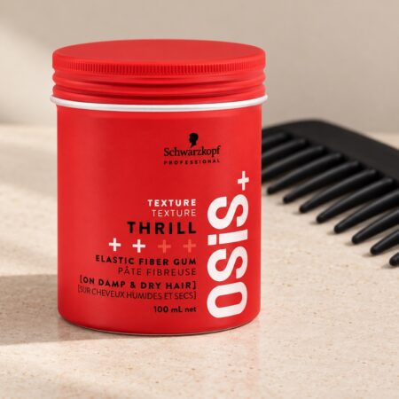 Czerwony słoiczek Schwarzkopf OSiS Thrill 100 ml przy czarnym grzebieniu na jasnym blacie