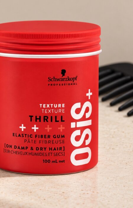 Czerwony słoiczek Schwarzkopf OSiS Thrill 100 ml przy czarnym grzebieniu na jasnym blacie