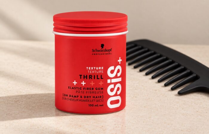 Czerwony słoiczek Schwarzkopf OSiS Thrill 100 ml przy czarnym grzebieniu na jasnym blacie