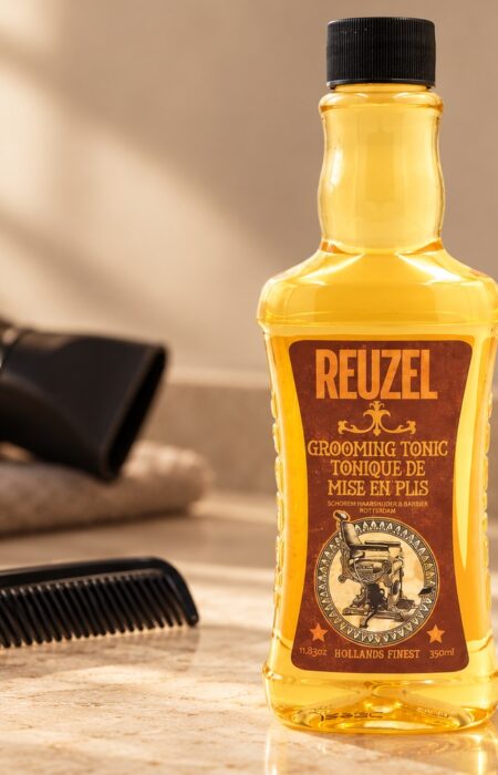 Butelka Reuzel Grooming Tonic 350 ml obok grzebienia na jasnym blacie