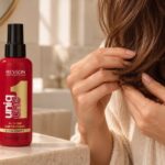 Czerwona butelka Revlon UniqOne obok kobiety układającej końce brązowych włosów.
