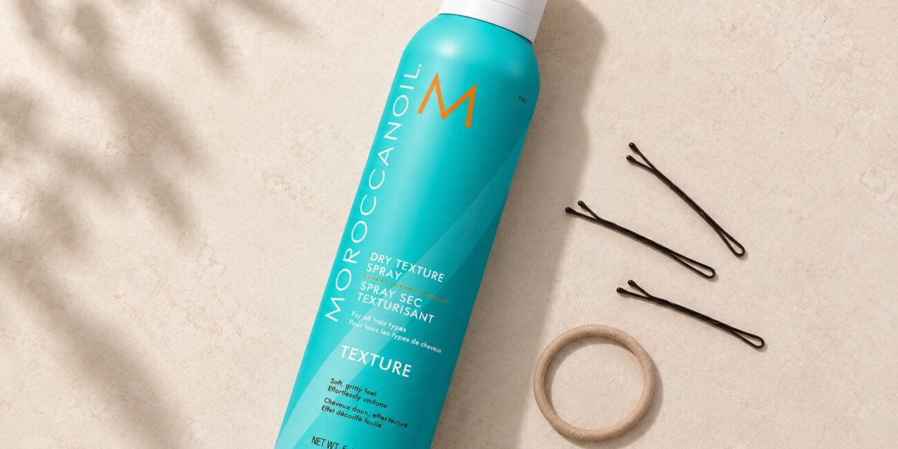 Turkusowy spray Moroccanoil Dry Texture 205 ml z białą nasadką obok wsuwek i gumki.
