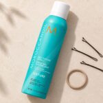 Turkusowy spray Moroccanoil Dry Texture 205 ml z białą nasadką obok wsuwek i gumki.