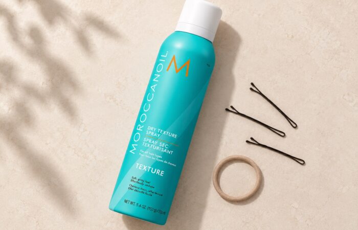 Turkusowy spray Moroccanoil Dry Texture 205 ml z białą nasadką obok wsuwek i gumki.