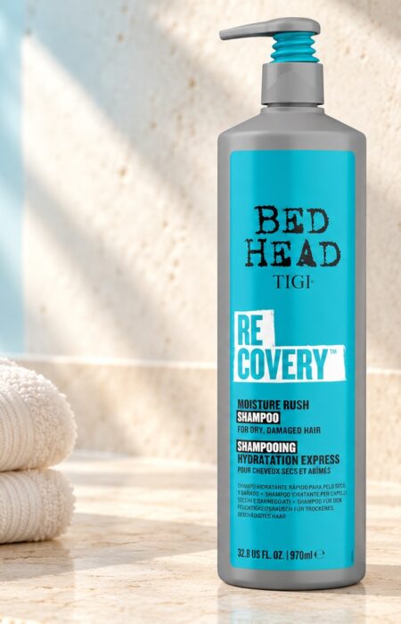 Szara butelka TIGI Bed Head Recovery 970 ml z turkusową etykietą obok jasnych ręczników