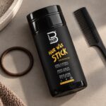Czarny sztyft L3VEL3 Hair Wax Stick 75 g obok grzebienia i miękkiej gumki do włosów.
