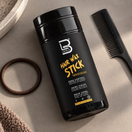 Czarny sztyft L3VEL3 Hair Wax Stick 75 g obok grzebienia i miękkiej gumki do włosów.