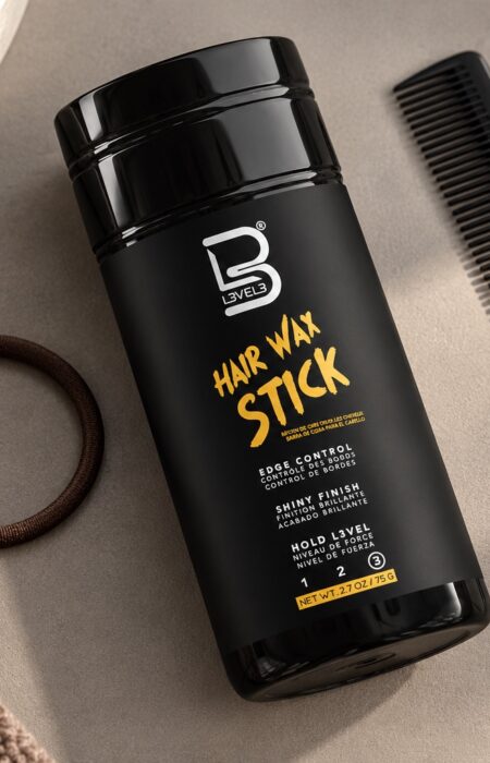 Czarny sztyft L3VEL3 Hair Wax Stick 75 g obok grzebienia i miękkiej gumki do włosów.