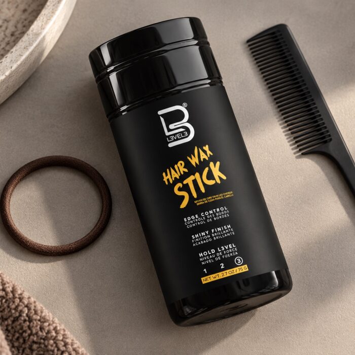 Czarny sztyft L3VEL3 Hair Wax Stick 75 g obok grzebienia i miękkiej gumki do włosów.